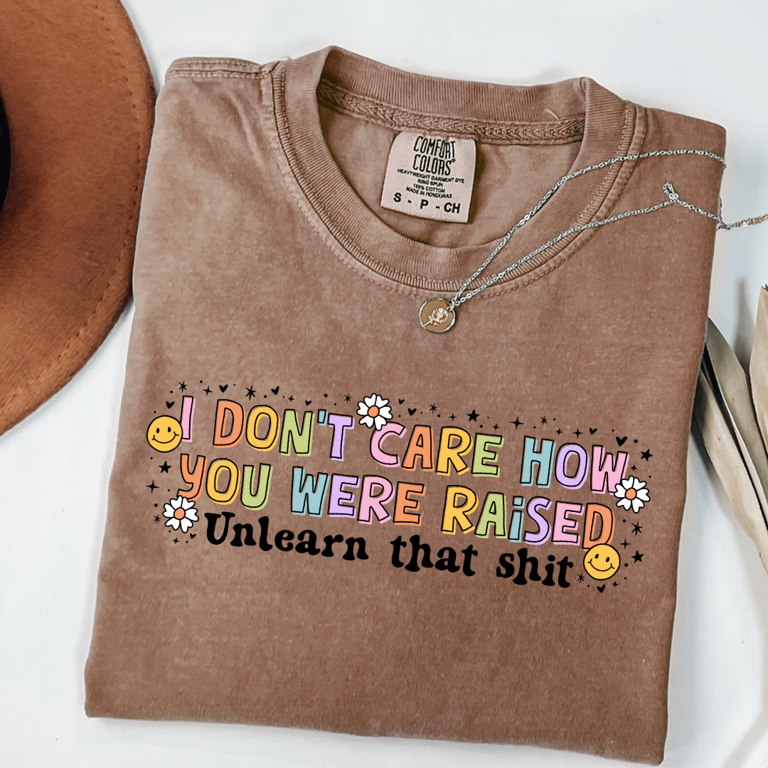Customized Adult Comfort Colors Espresso Brown Graphic Tee " I don't care how you were raised" rainbow capital letters Unlearn that shit Black bubble letters. Smiley faces and flowers around. good for pride month matching adult crewnecks and hoodies available.
