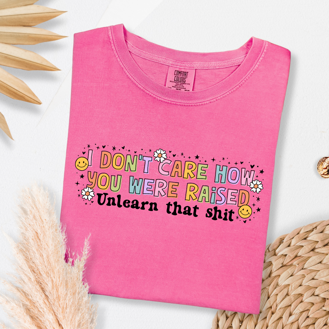 Customized Adult Comfort Colors Crunchberry Pink Graphic Tee " I don't care how you were raised" rainbow capital letters Unlearn that shit Black bubble letters. Smiley faces and flowers around. good for pride month matching adult crewnecks and hoodies available.