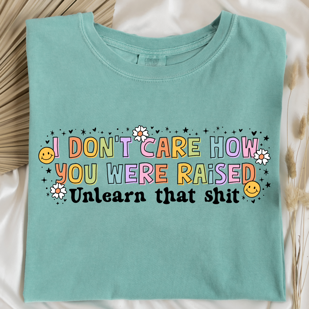 Customized Adult Comfort Colors Chalky Mint Graphic Tee " I don't care how you were raised" rainbow capital letters Unlearn that shit Black bubble letters. Smiley faces and flowers around. good for pride month matching adult crewnecks and hoodies available.