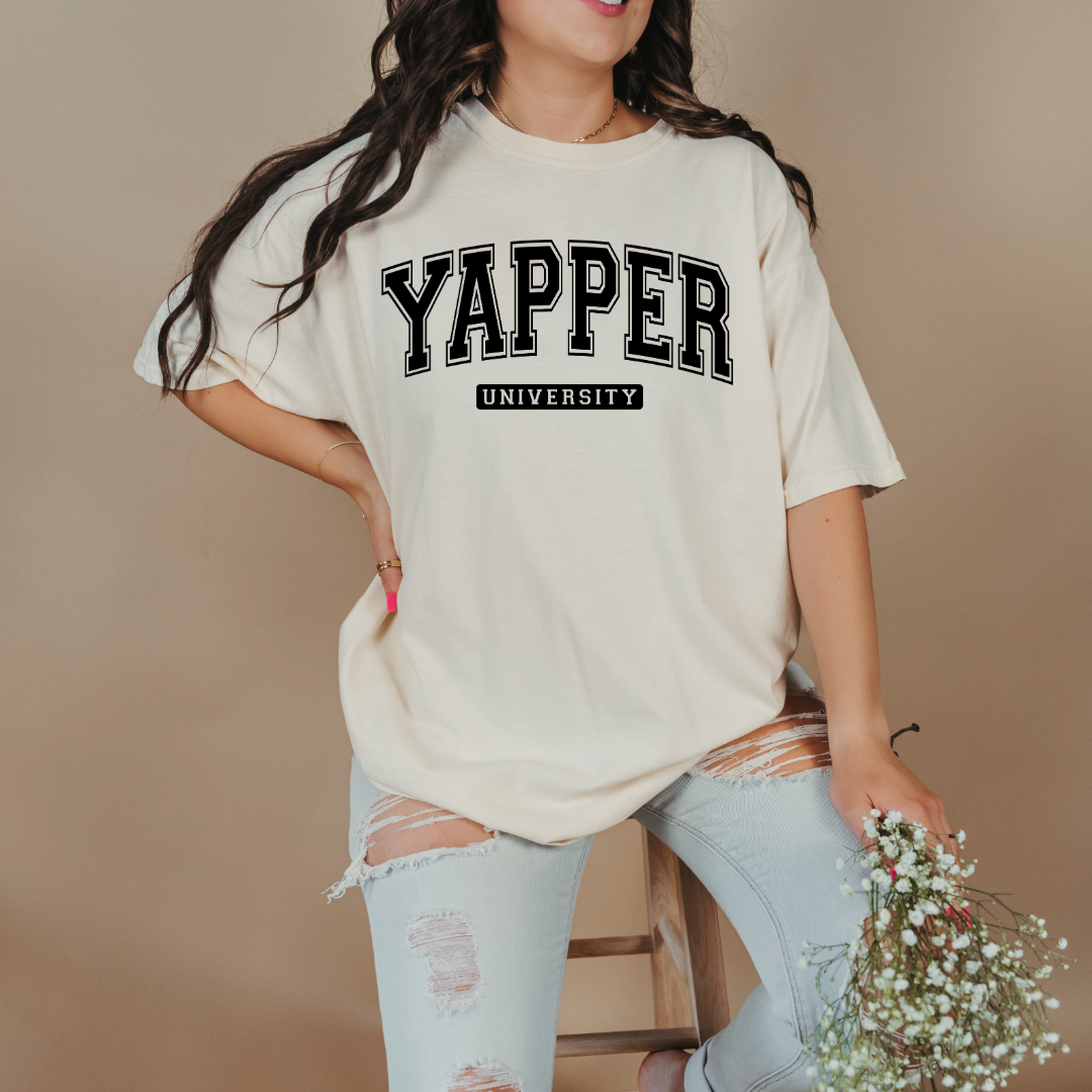 Customized adult comfort colors ivory Graphic tee with black varsity lettering yapper university Matching hoodies and crewnecks in adult and youth sizes available.