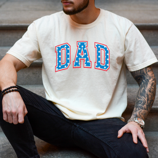Customized adult Comfort Colors Ivory Graphic Tee  with Seasonal 4th of July University style Font DAD blue with white stars outlined un red , This style is available in adult  Graphic Tees as well as adult crewnecks and hoodies .Available In DAD, MAMA and MINI.