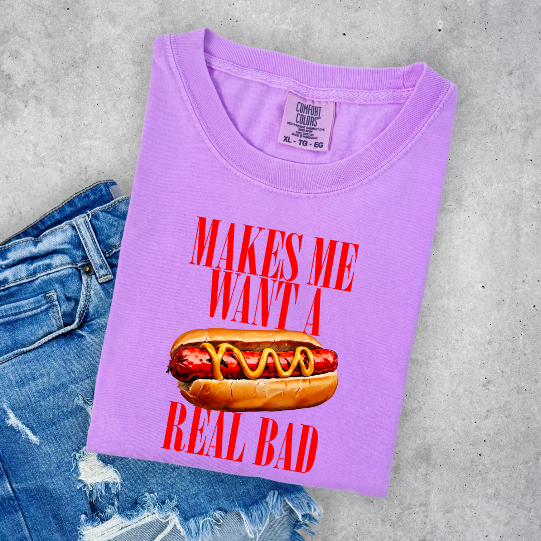 Customized Comfort Colors Neon Violet Graphic Tee big red block letters " makes me \want a hot dog real bad with a picture of a hotdog in the middle. Jennifer Coolidge quote legally blonde. Available in sizes Youth Small through adult 4X available in matching Crewnecks and adult hoodies as well.