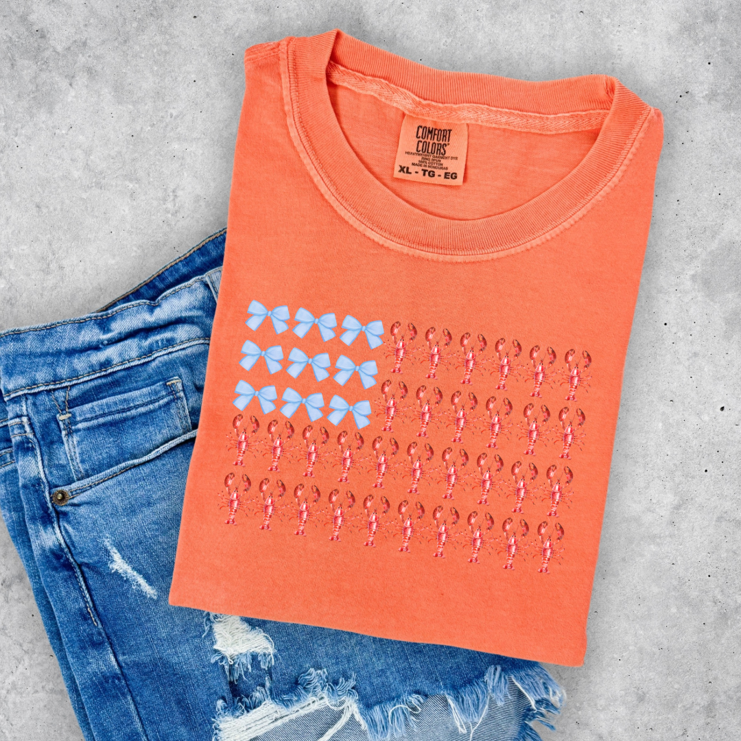 Customized comfort colors Youth Melon Orange Graphic tee with American Flag made of blue bows and red lobsters. Perfect for 4th of July Ranging in sizes youth Small to adult 4X also comes in matching hoodies and crewnecks.