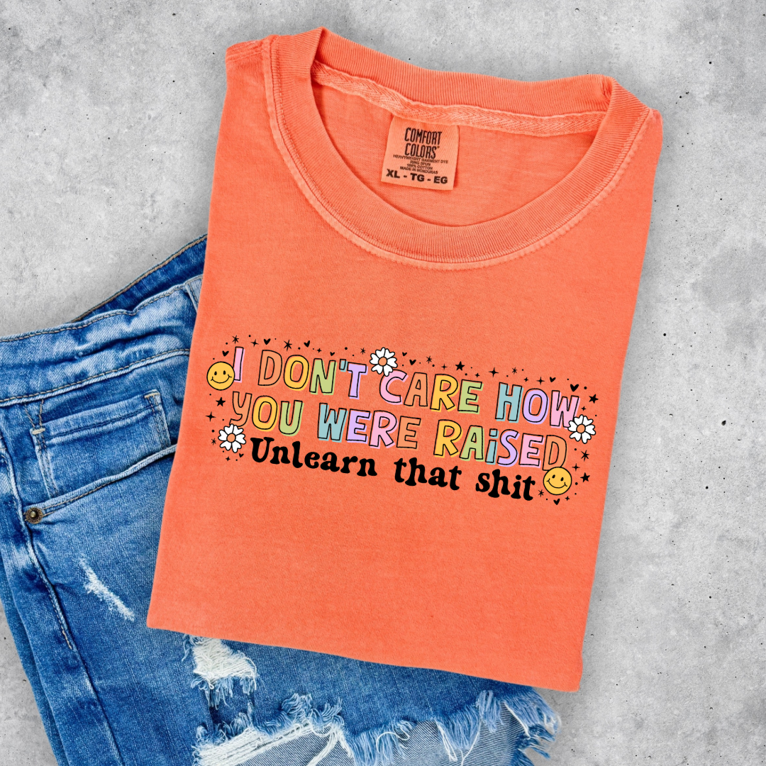 Customized Adult Comfort Colors Melon Orange Graphic Tee " I don't care how you were raised" rainbow capital letters Unlearn that shit Black bubble letters. Smiley faces and flowers around. good for pride month matching adult crewnecks and hoodies available. 