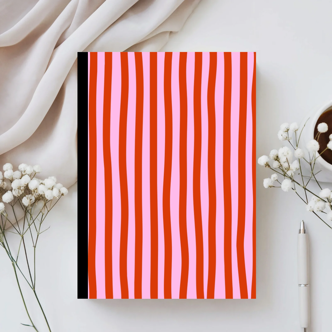 Notebook with red and pink striped cover on a white surface with flowers and a pen.