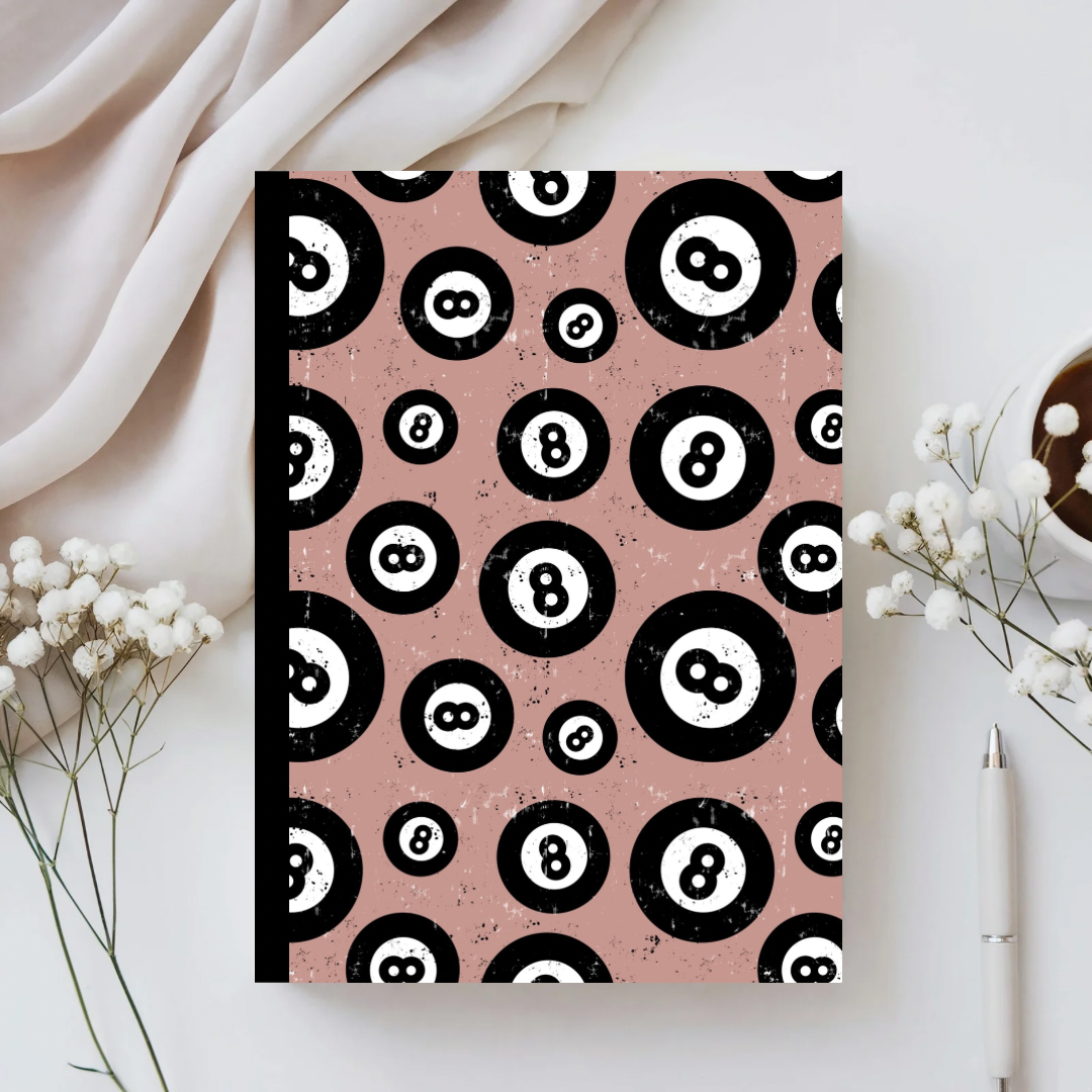 Notebook with black and white pattern on pink cover, placed on a light surface with decorative elements.