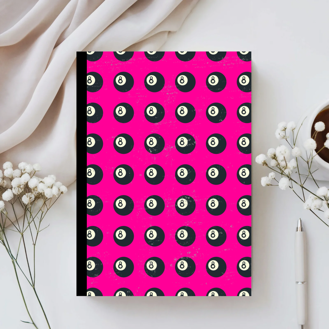 Notebook with pool ball pattern on pink cover, placed on a light surface with decorative elements.