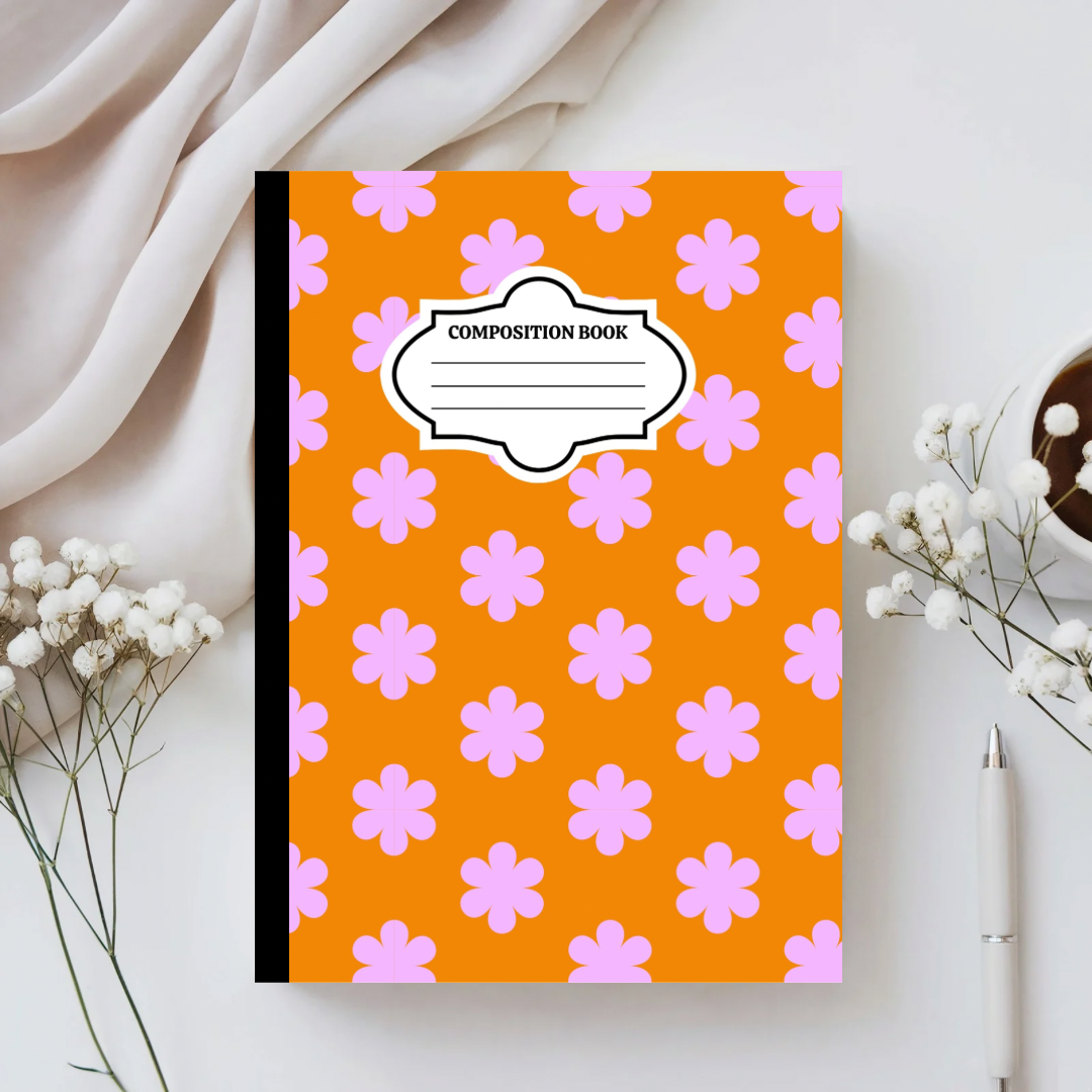 Composition book with pink flower pattern on an orange background, placed on a light surface with white flowers and a pen.