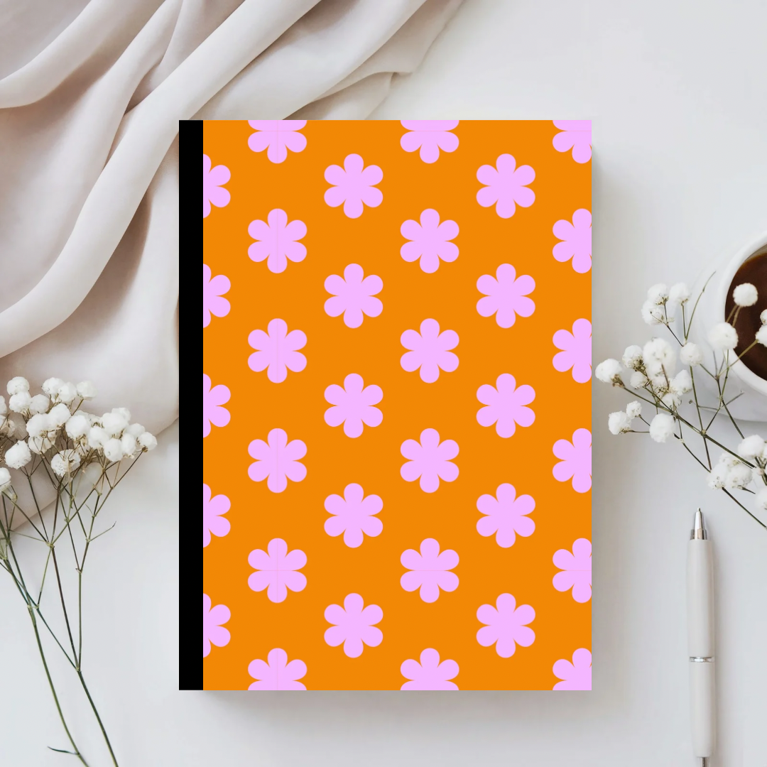 Notebook with pink flower pattern on an orange background, placed on a white surface with decorative elements.