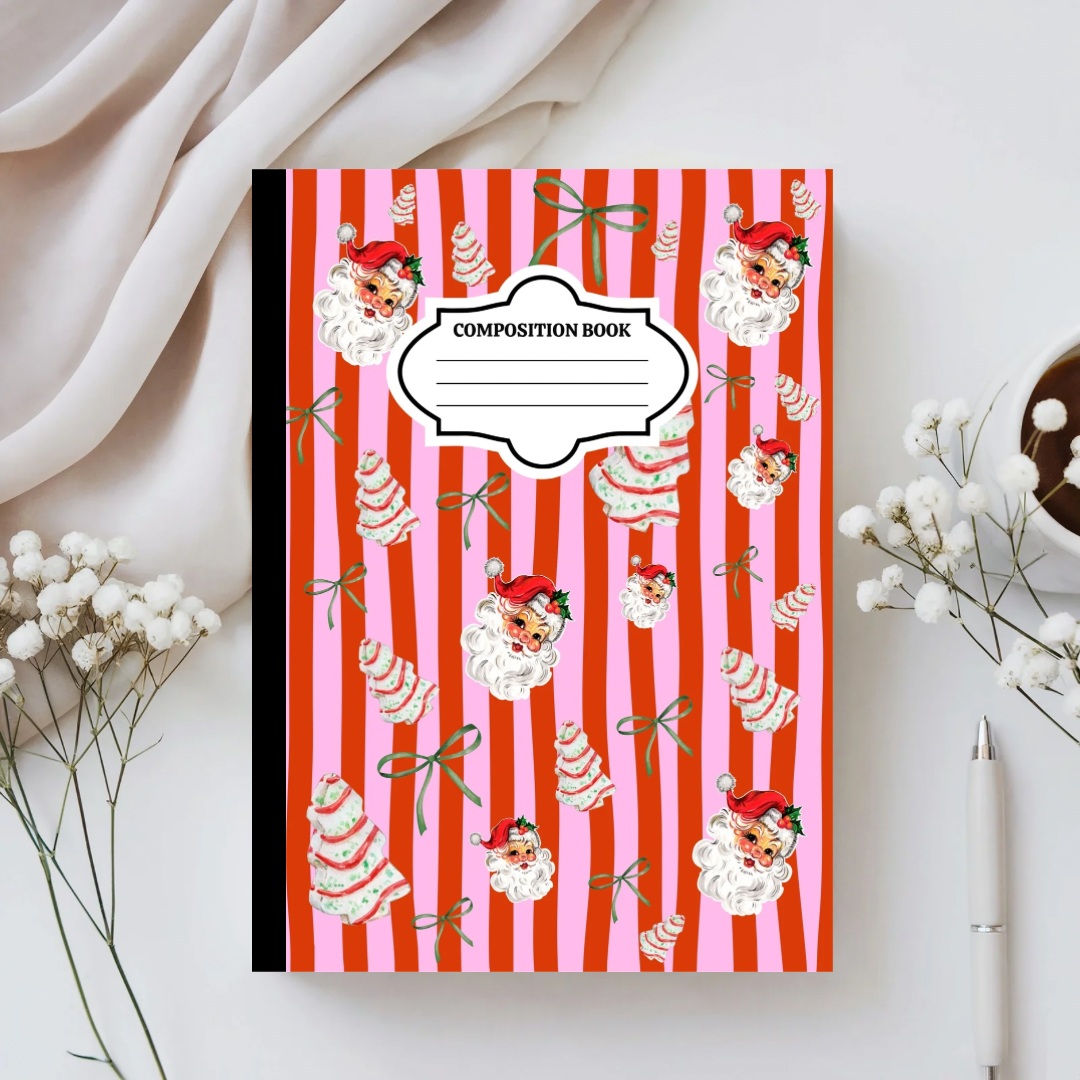 Composition book with Santa Claus and candy cane design on a white surface with flowers and a pen.