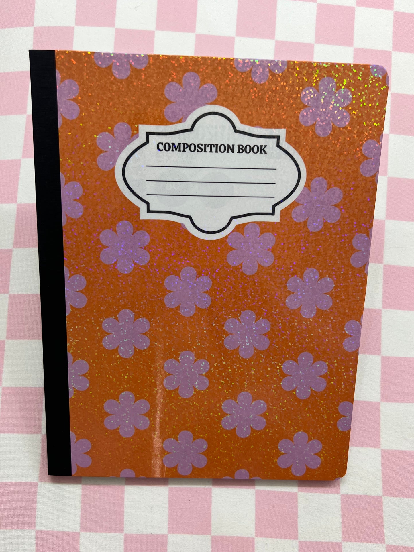 Composition book with purple flower pattern on a pink and white checkered background