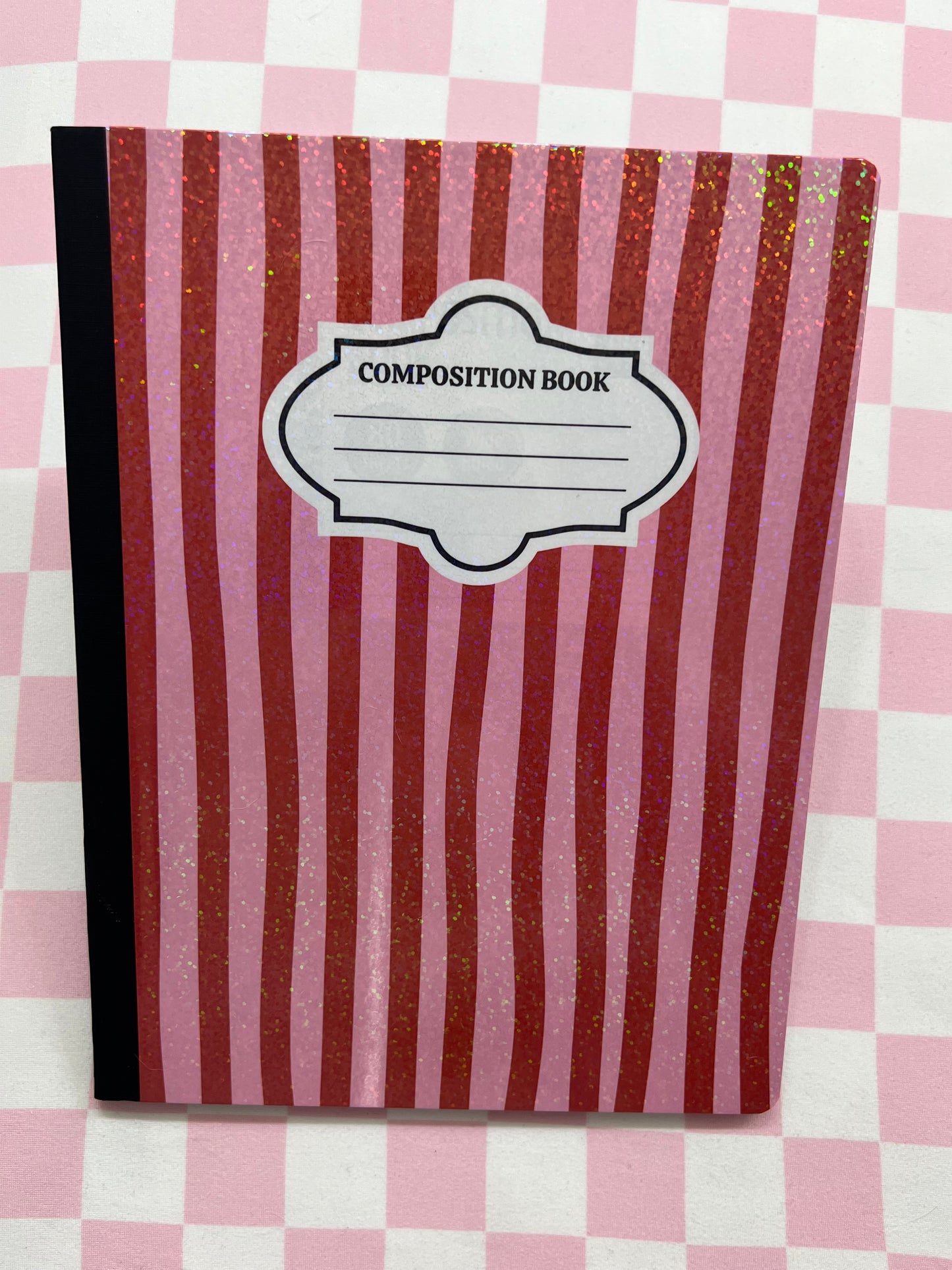 Composition book with red and white striped cover on a pink and white checkered background