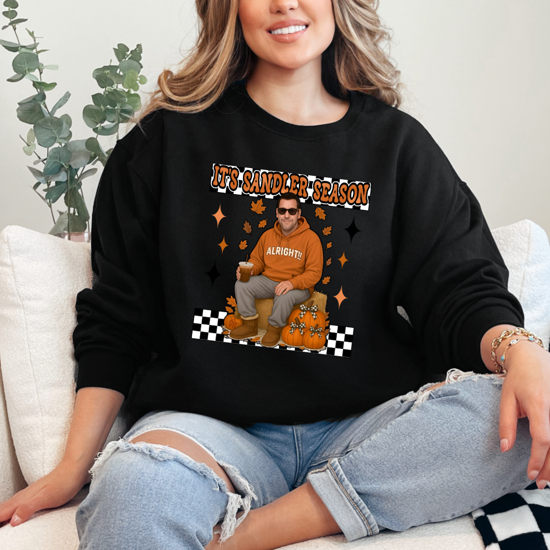 Black Adult Crewneck with Adam Sandler on the front sitting on a hay bale stack with a coffee in hand wearing UGGS and checker board its Sandler season. Design available in graphic tees as well in Adult sizing ranging from Small to 4X.