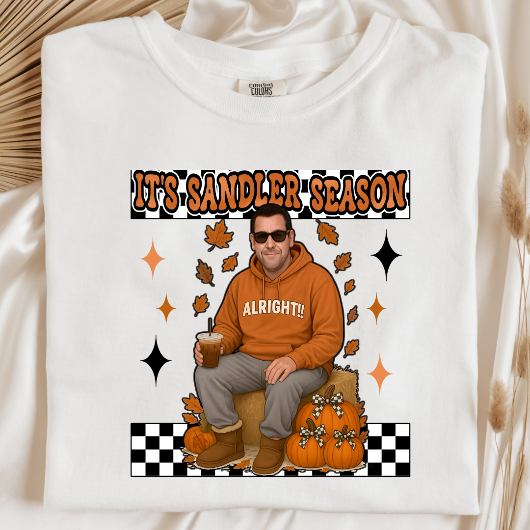Comfort Colors white Adult Graphic Tee with Adam Sandler on the front sitting on a hay bale stack with a coffee in hand wearing UGGS and checker board its Sandler season. Design available in graphic tees as well in Adult sizing ranging from Small to 4X.