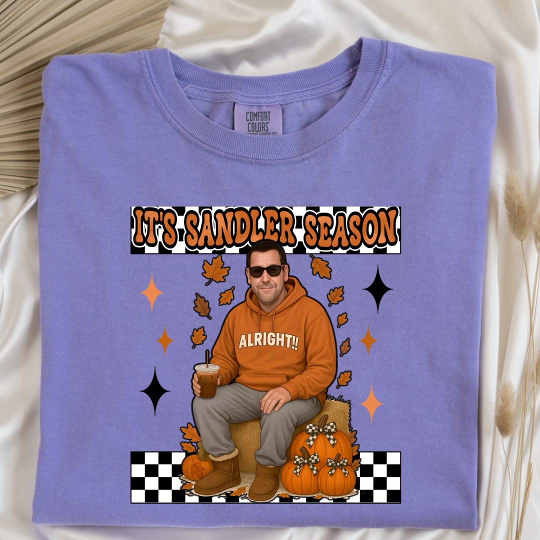 Comfort Colors Violet Adult Graphic Tee with Adam Sandler on the front sitting on a hay bale stack with a coffee in hand wearing UGGS and checker board its Sandler season. Design available in graphic tees as well in Adult sizing ranging from Small to 4X.