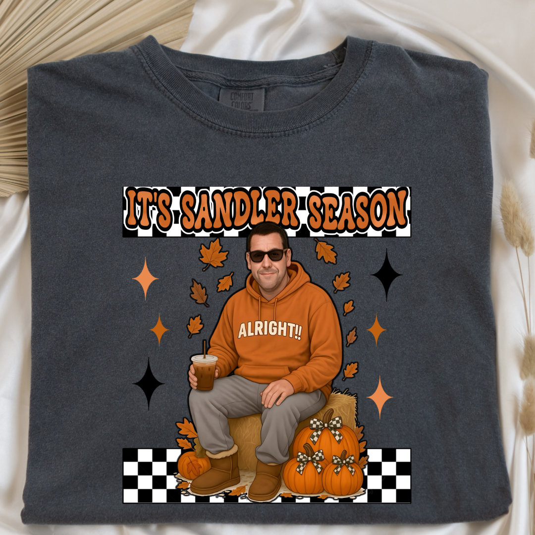 Comfort Colors Pepper Vintage Black Adult Graphic Tee with Adam Sandler on the front sitting on a hay bale stack with a coffee in hand wearing UGGS and checker board its Sandler season. Design available in graphic tees as well in Adult sizing ranging from Small to 4X.