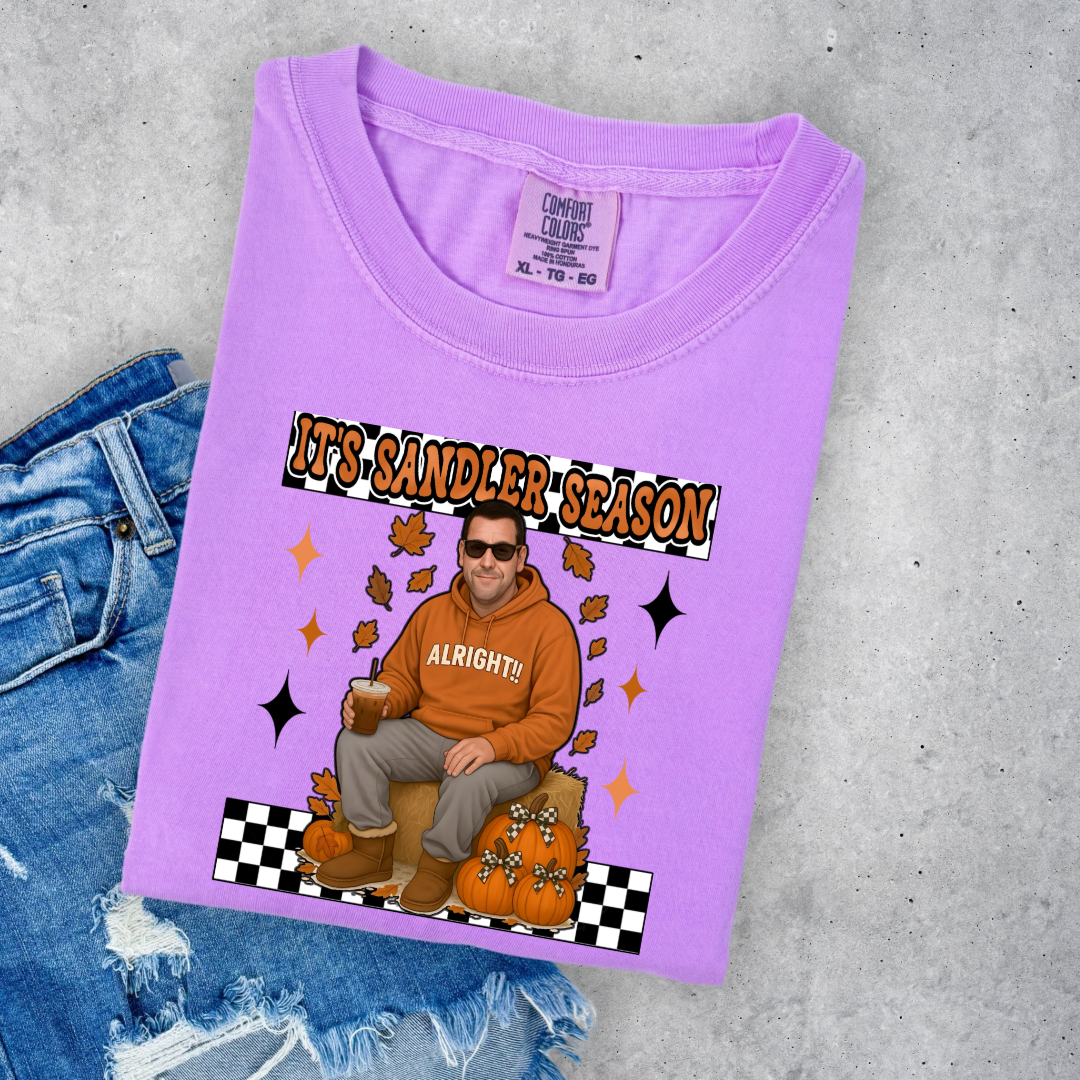 Comfort Colors Neon Violet Adult Graphic Tee with Adam Sandler on the front sitting on a hay bale stack with a coffee in hand wearing UGGS and checker board its Sandler season. Design available in graphic tees as well in Adult sizing ranging from Small to 4X.