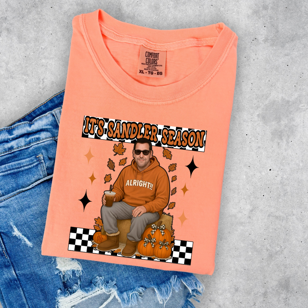 Comfort Colors Neon Cantaloupe Adult Graphic Tee with Adam Sandler on the front sitting on a hay bale stack with a coffee in hand wearing UGGS and checker board its Sandler season. Design available in graphic tees as well in Adult sizing ranging from Small to 4X.