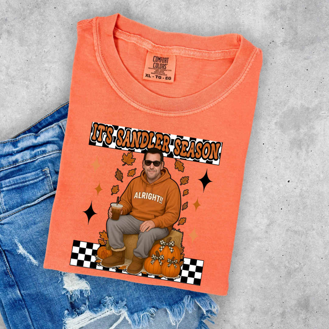 Comfort Colors Melon Orange Adult Graphic Tee with Adam Sandler on the front sitting on a hay bale stack with a coffee in hand wearing UGGS and checker board its Sandler season. Design available in graphic tees as well in Adult sizing ranging from Small to 4X.