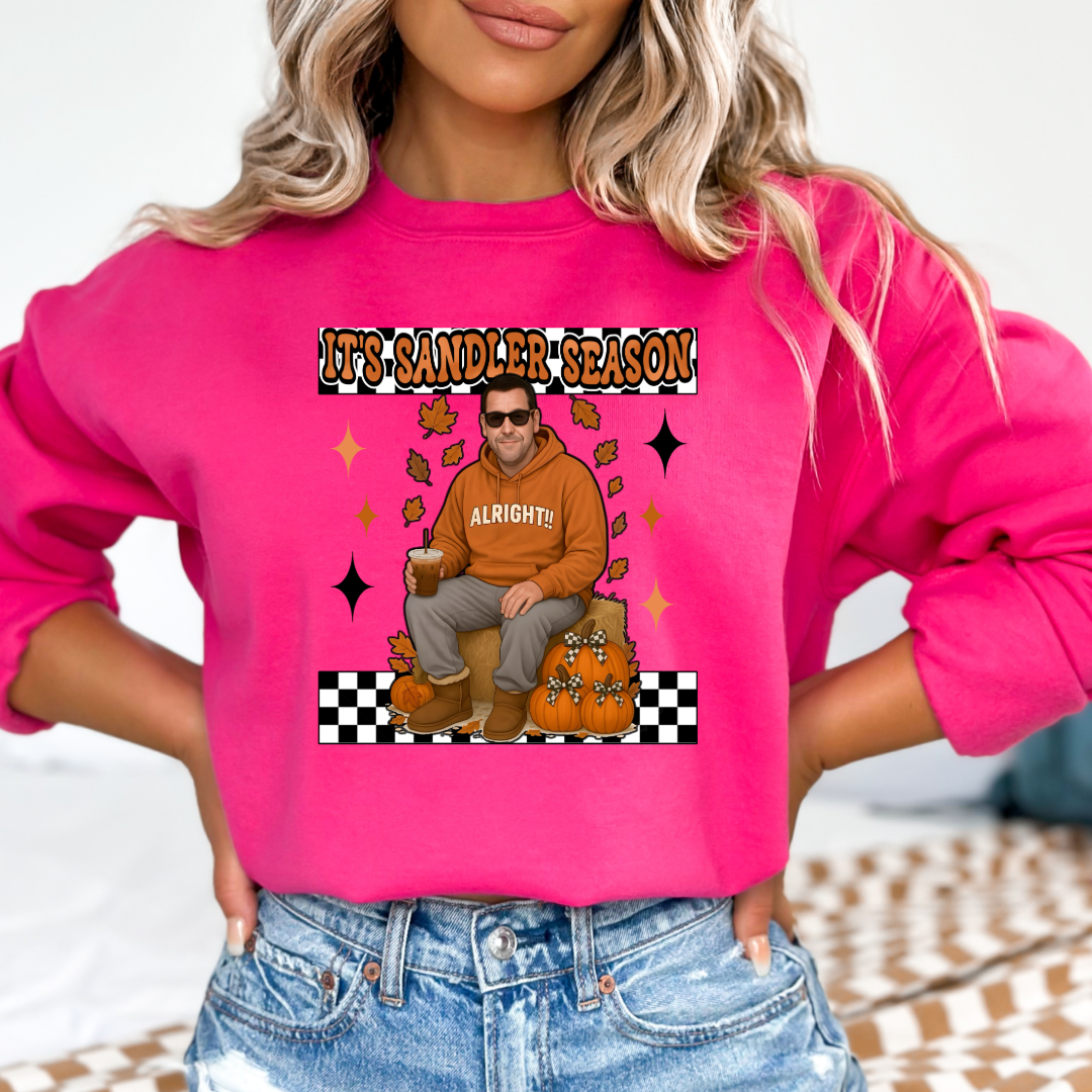 Hot Medium Pink Adult Crewneck with Adam Sandler on the front sitting on a hay bale stack with a coffee in hand wearing UGGS and checker board its Sandler season. Design available in graphic tees as well in Adult sizing ranging from Small to 4X.