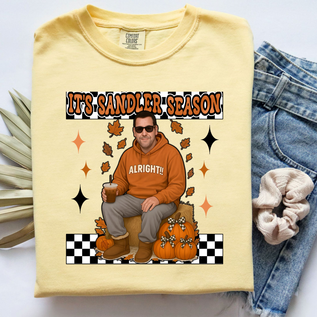 Comfort Colors Butter Adult Graphic Tee with Adam Sandler on the front sitting on a hay bale stack with a coffee in hand wearing UGGS and checker board its Sandler season. Design available in graphic tees as well in Adult sizing ranging from Small to 4X.