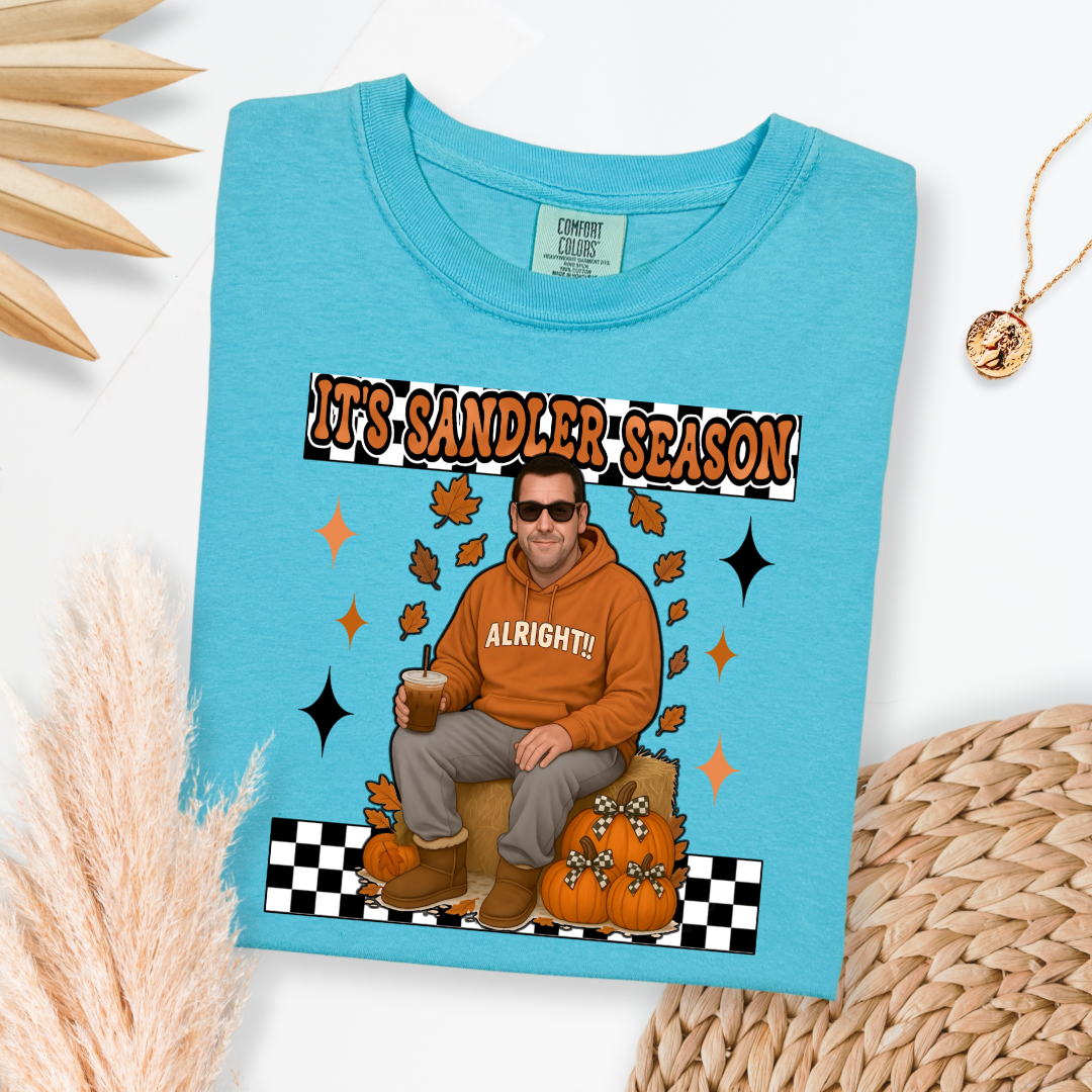 Comfort Colors Lagoon Blue Adult Graphic Tee with Adam Sandler on the front sitting on a hay bale stack with a coffee in hand wearing UGGS and checker board its Sandler season. Design available in graphic tees as well in Adult sizing ranging from Small to 4X.