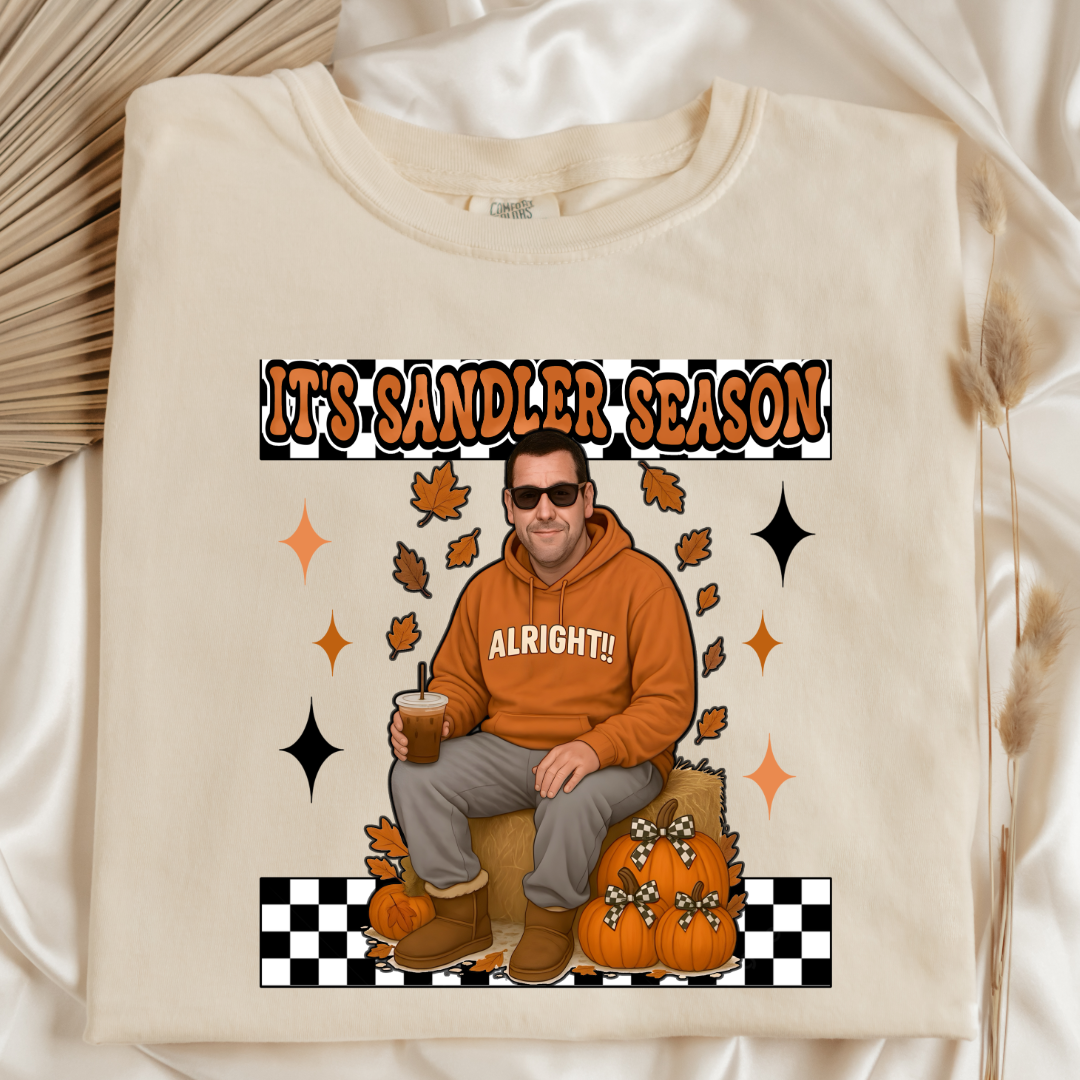 Comfort Colors Ivory folded flat lay Adult Graphic Tee with Adam Sandler on the front sitting on a hay bale stack with a coffee in hand wearing UGGS and checker board its Sandler season. Design available in graphic tees as well in Adult sizing ranging from Small to 4X.