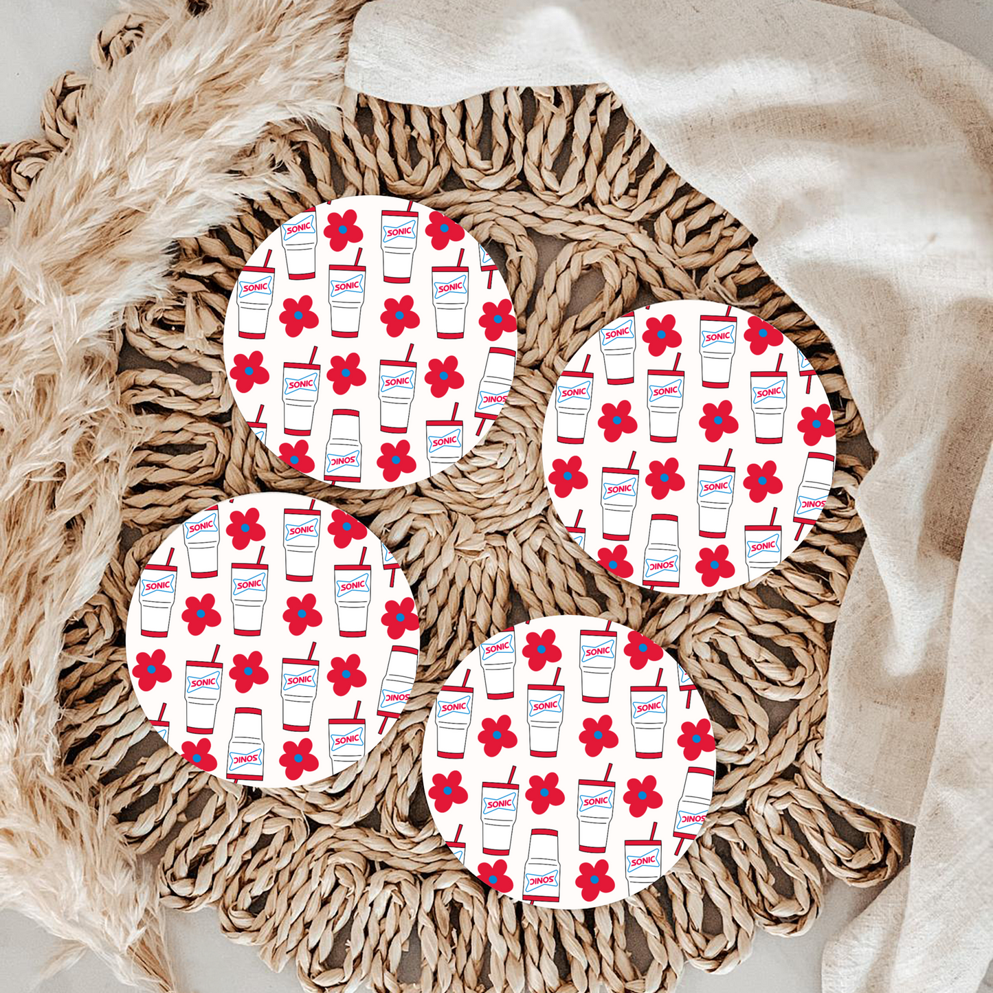 Four circular coasters with a floral and drink pattern on a textured surface.