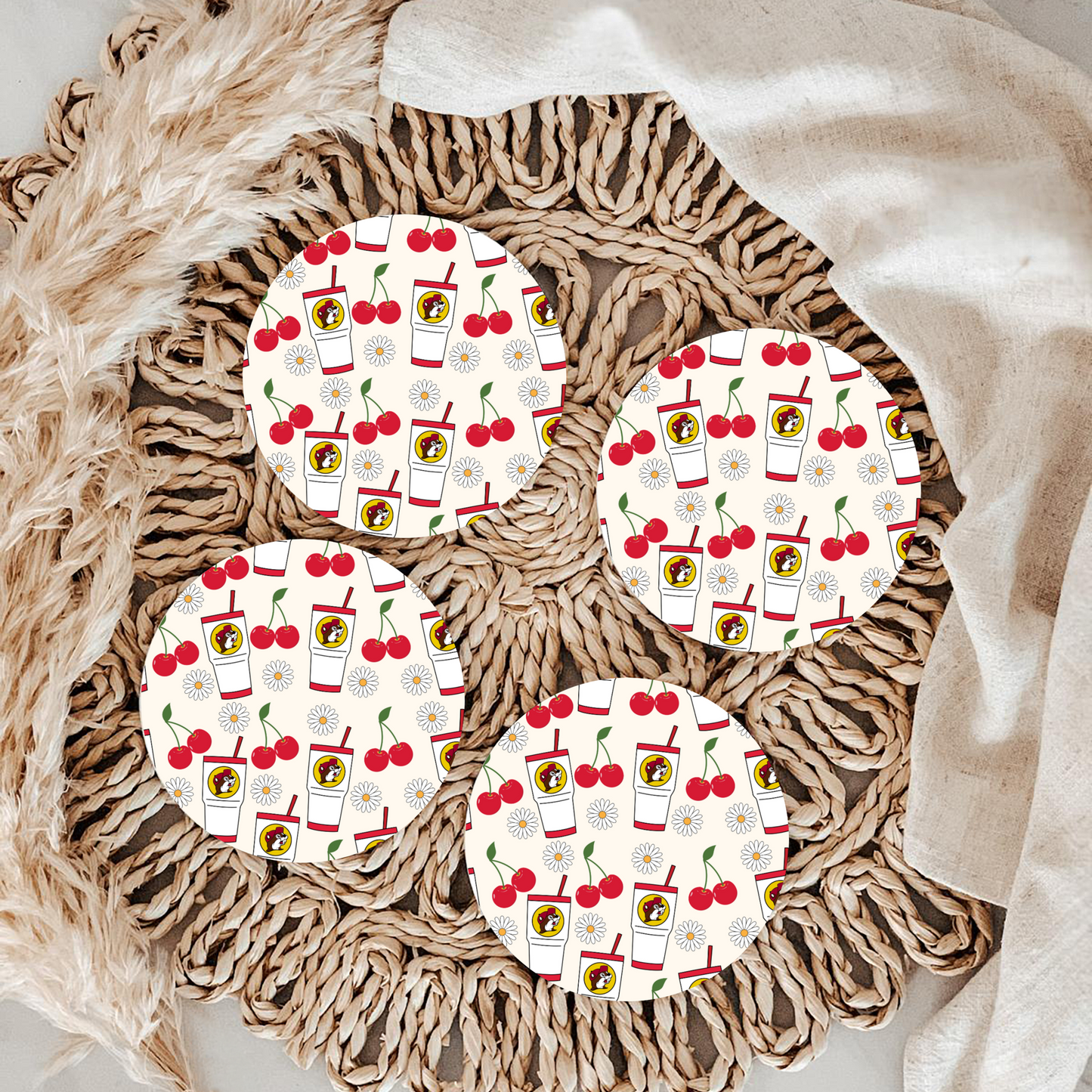 Four round coasters with a cherry and drink pattern on a woven surface.
