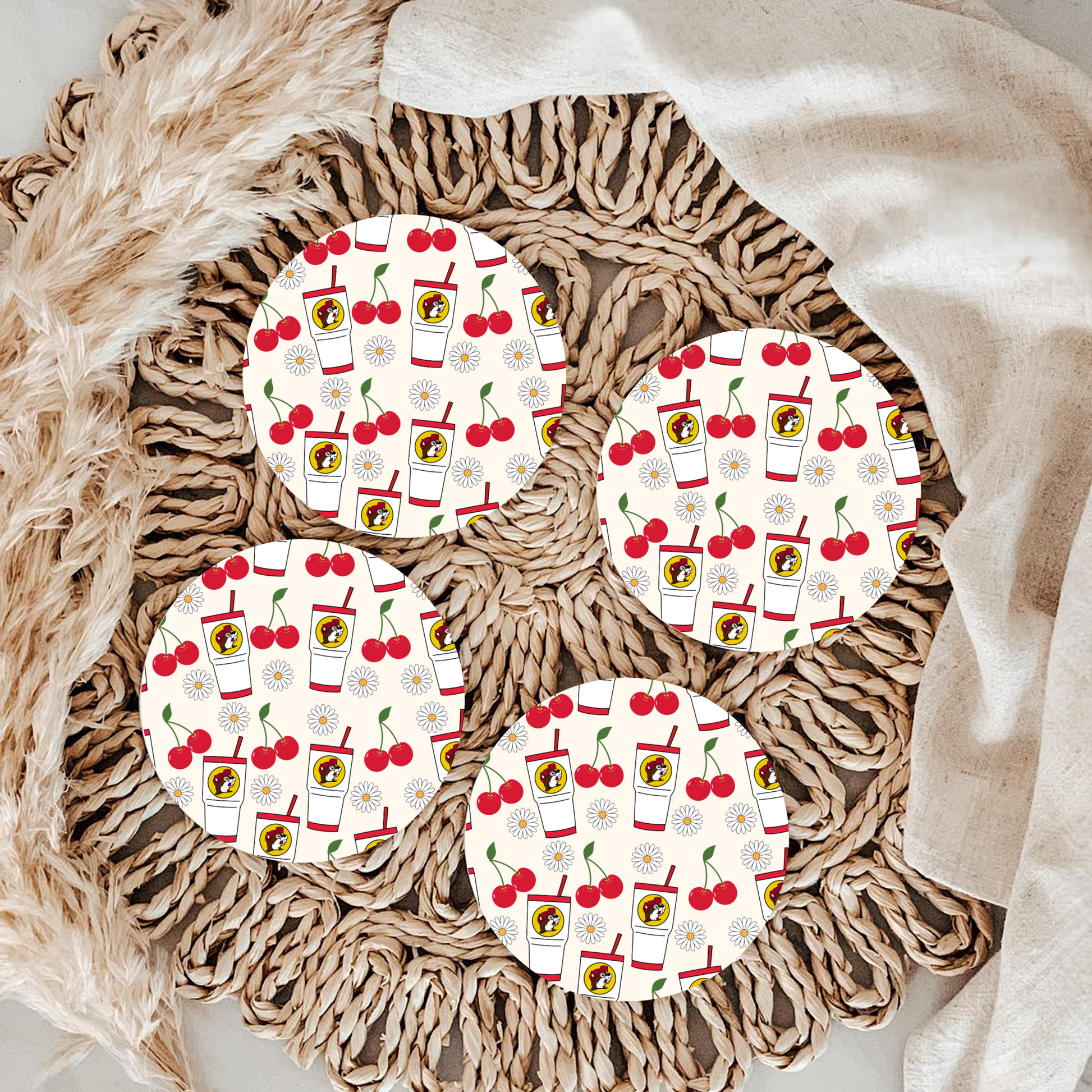 Four round coasters with a cherry and drink pattern on a woven surface.