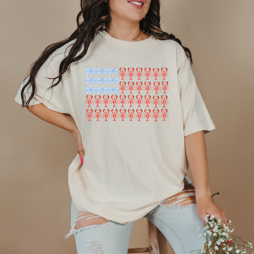 Customized comfort colors ivory Graphic tee with American Flag made of blue bows and red lobsters. Perfect for 4th of July Ranging in sizes youth Small to adult 4X also comes in matching hoodies and crewnecks. 